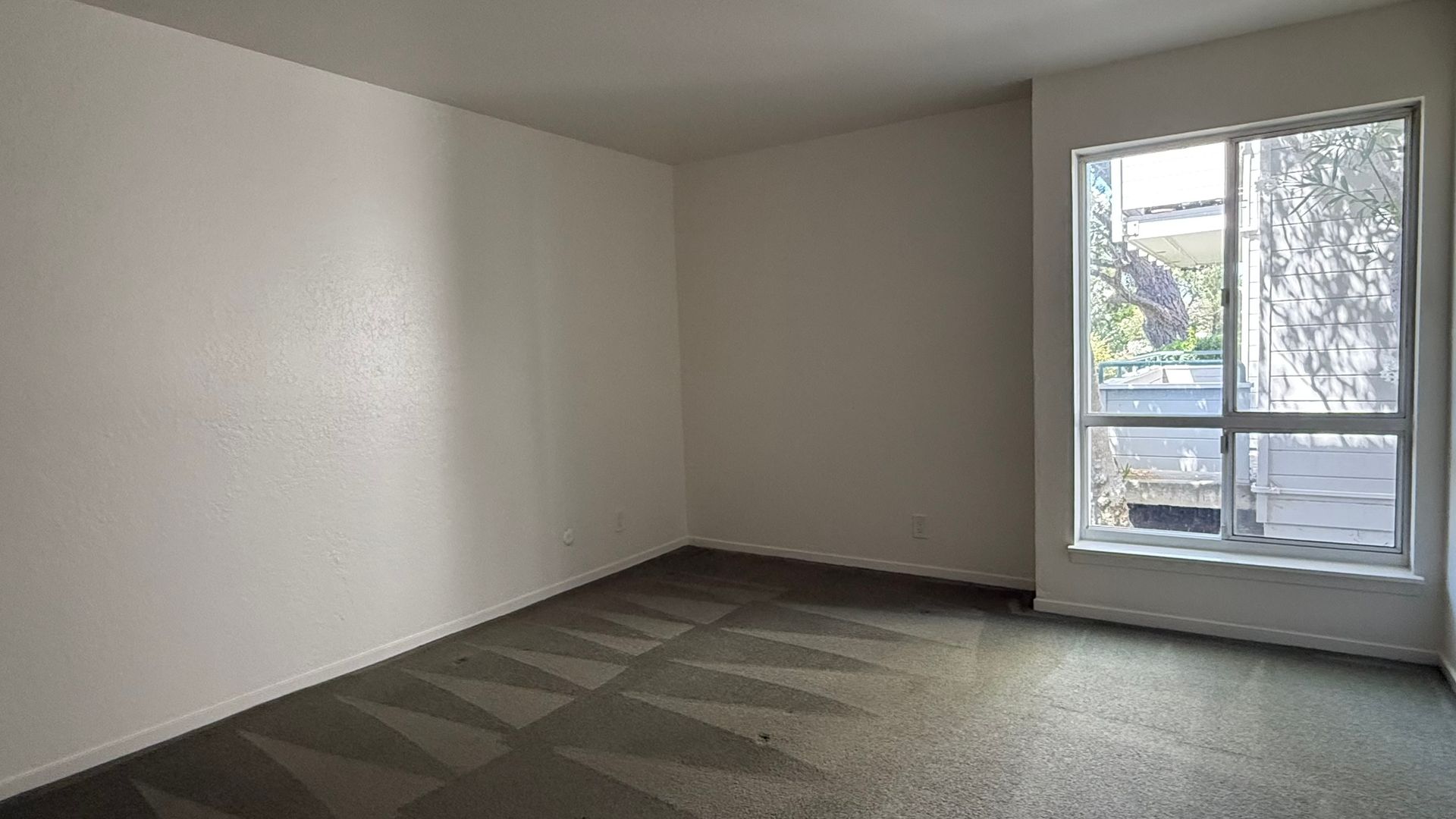 Empty room with white walls, gray carpet, and a large window.