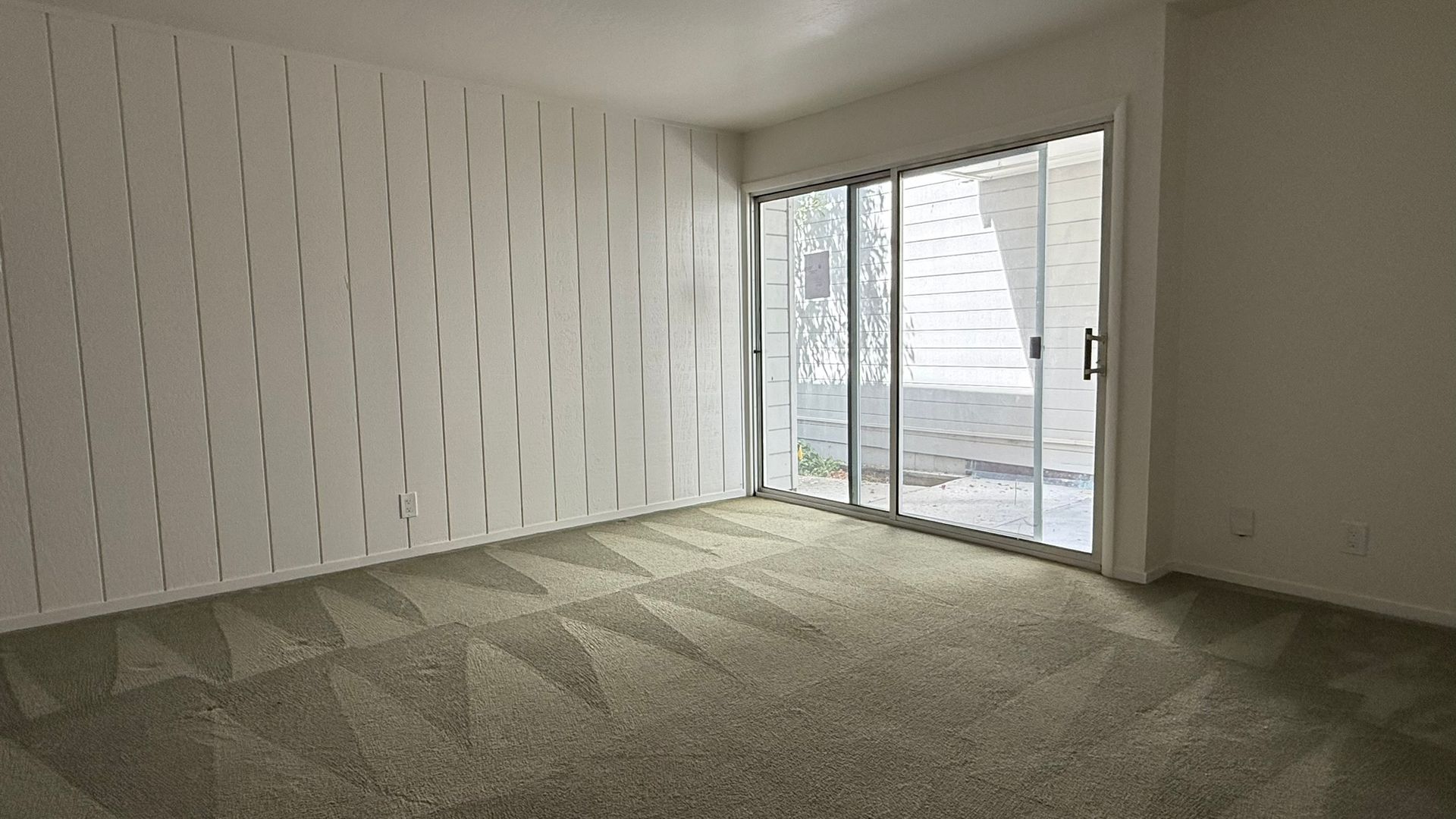 Empty room with patterned carpet, textured white wall, and sliding glass door.