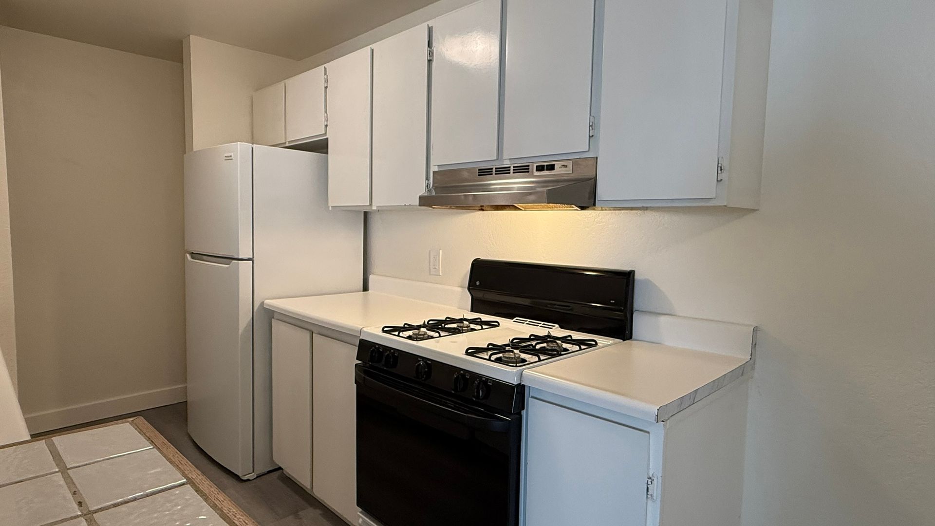 Small, white kitchen with white cabinets, stove, refrigerator, and countertop.