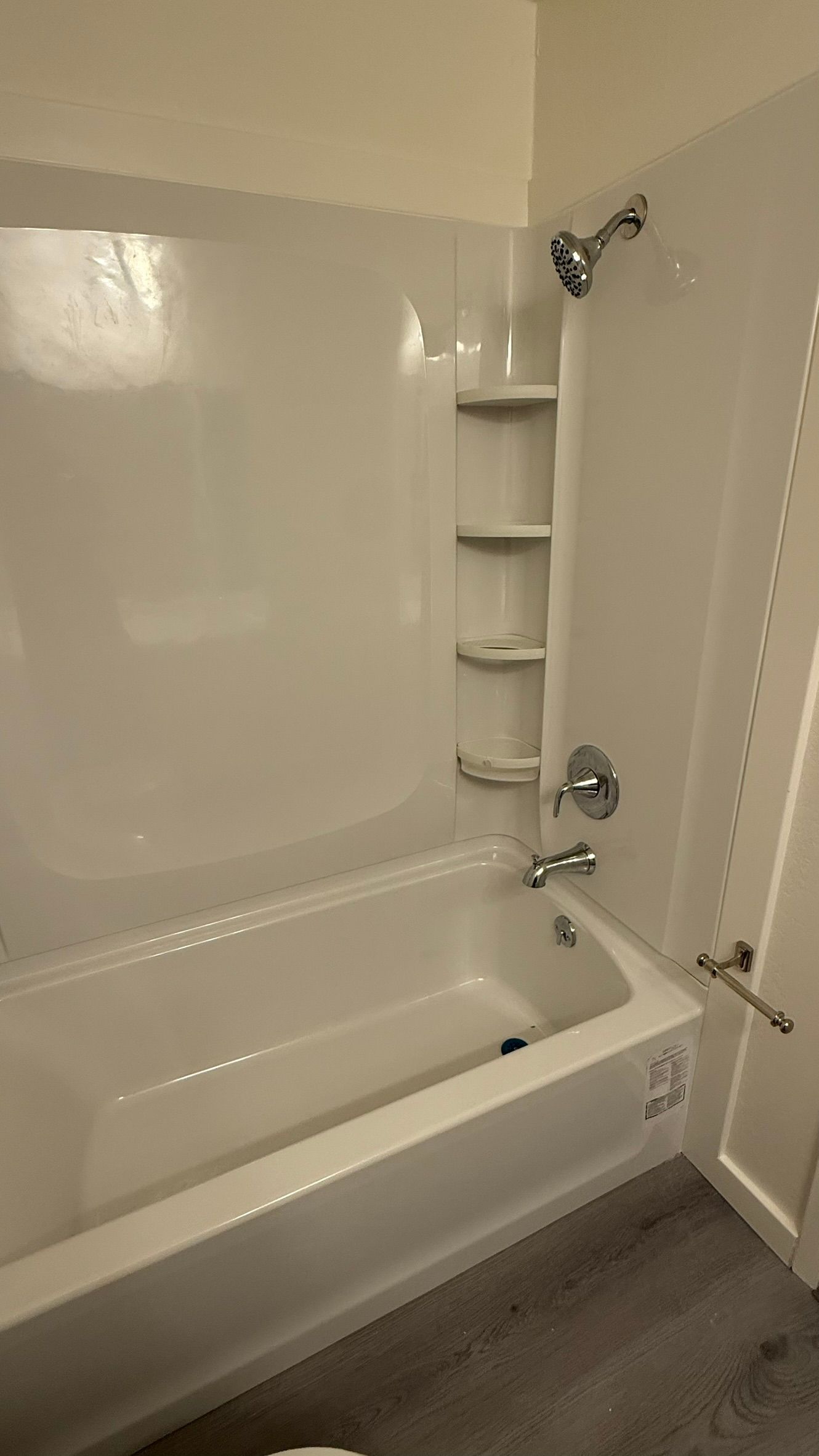 White bathtub and shower with built-in shelves. Silver fixtures, light-colored walls and floor.