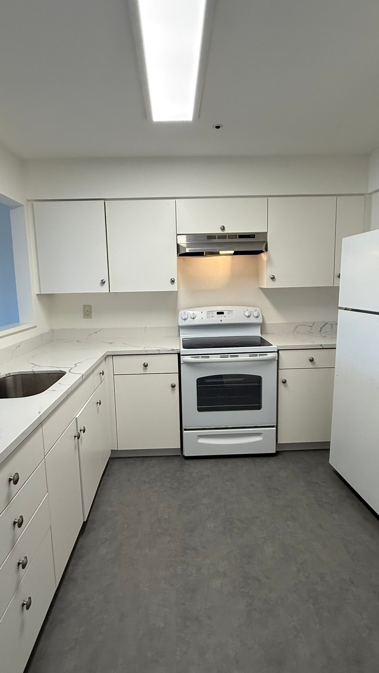 White kitchen with white cabinets, stove, and refrigerator; gray floor.