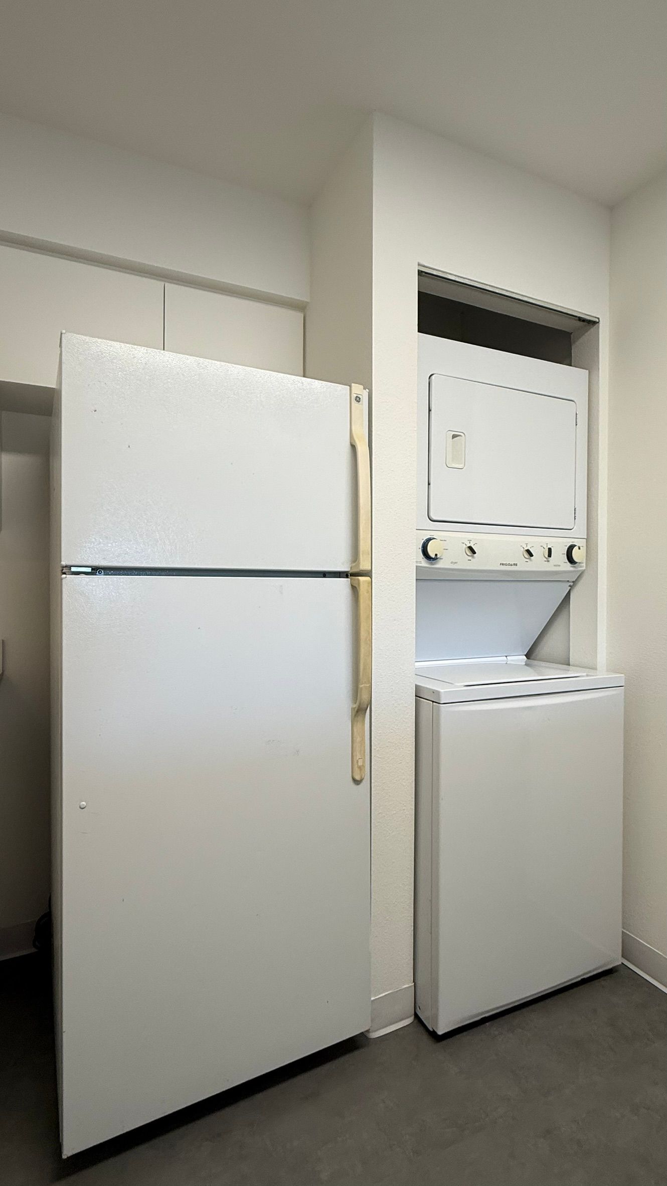 White refrigerator and stacked washer/dryer in a small room, gray flooring.