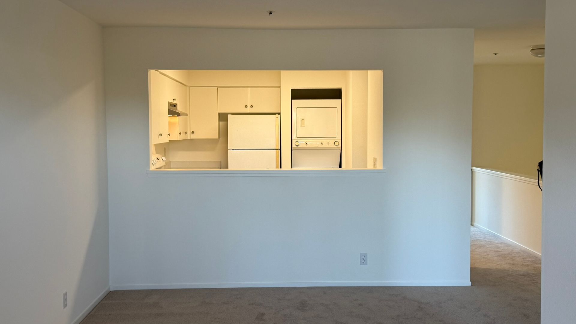 White interior with a pass-through to a kitchen with appliances and white cabinetry; carpeted floors.