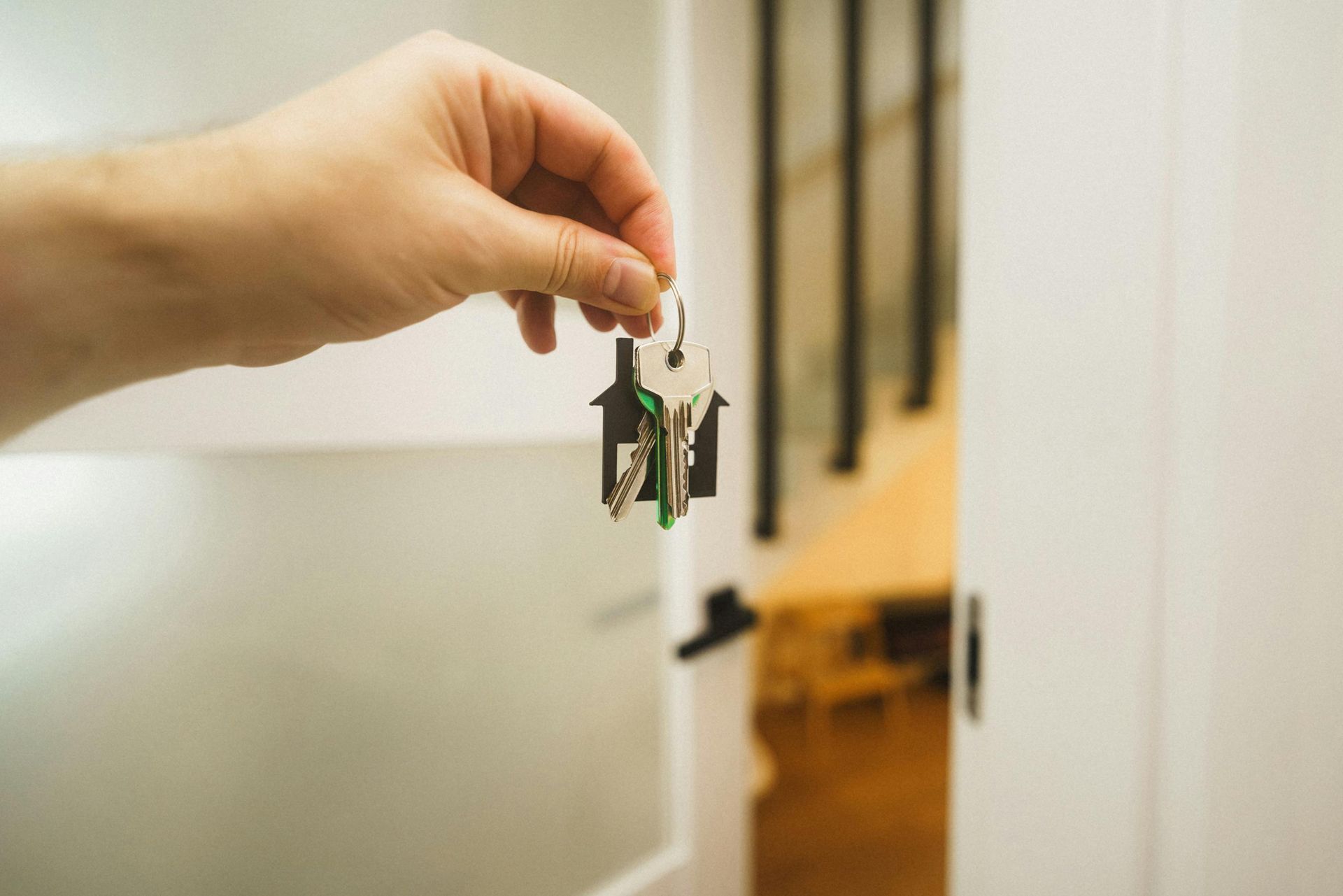 Hand holding keys in front of an open doorway; focus on the keys.