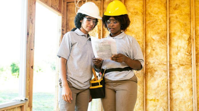 Two women wearing hard hats and safety glasses are standing next to each other in a room.