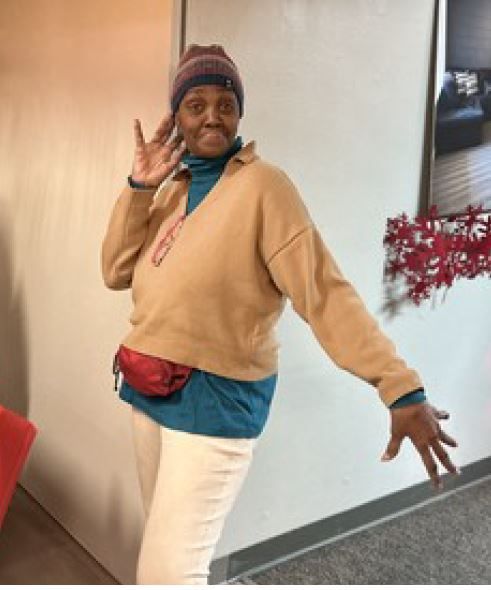 A woman wearing a hat and a sweater is standing in a room with her arms outstretched