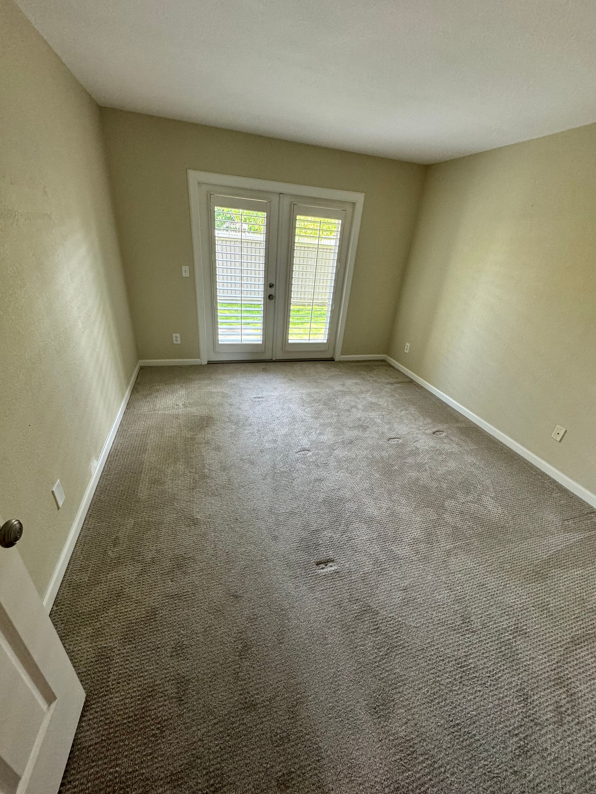 An empty room with a carpeted floor and sliding glass doors.