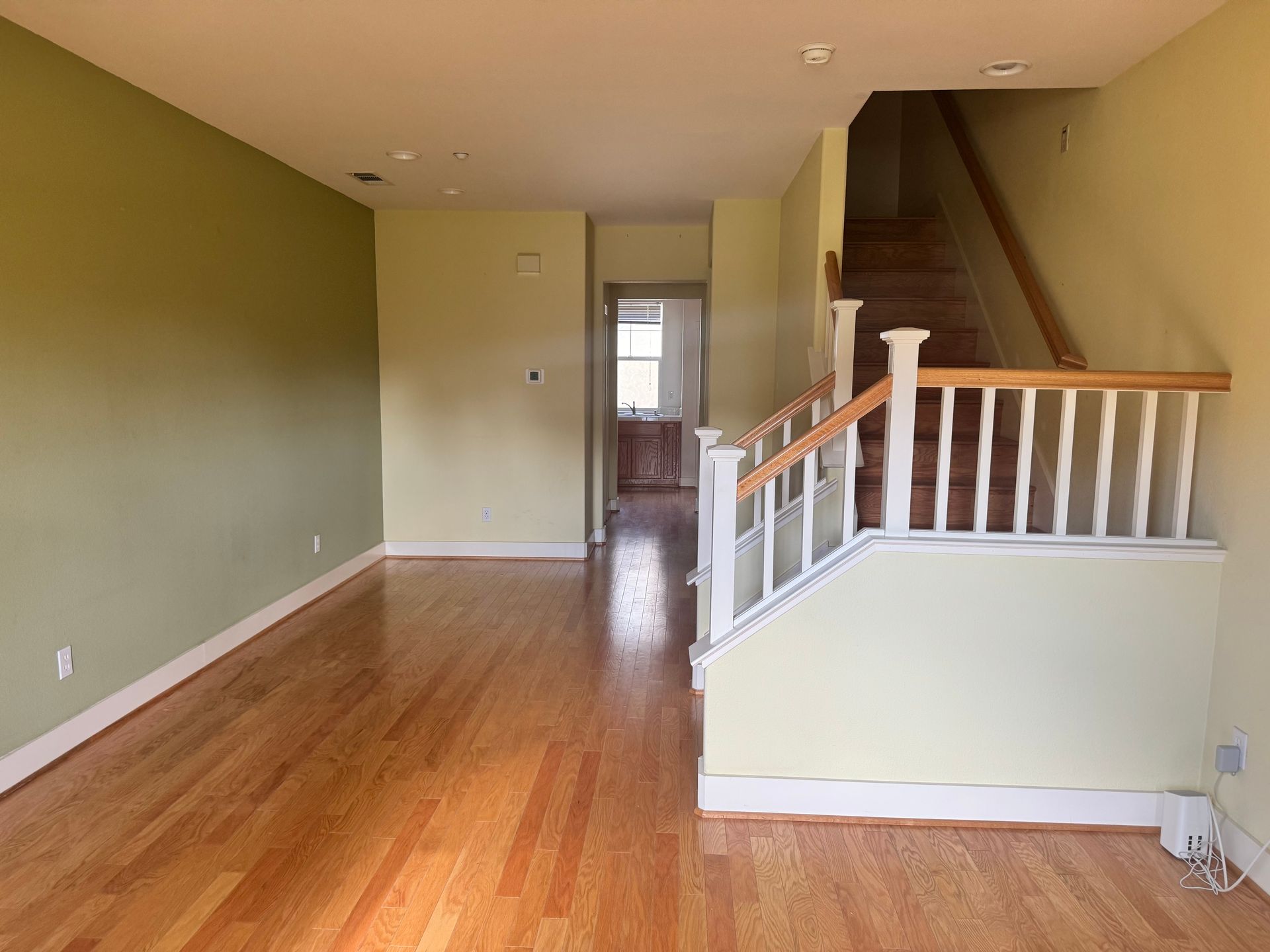 Empty living room with wood floors, staircase, and green and yellow walls.