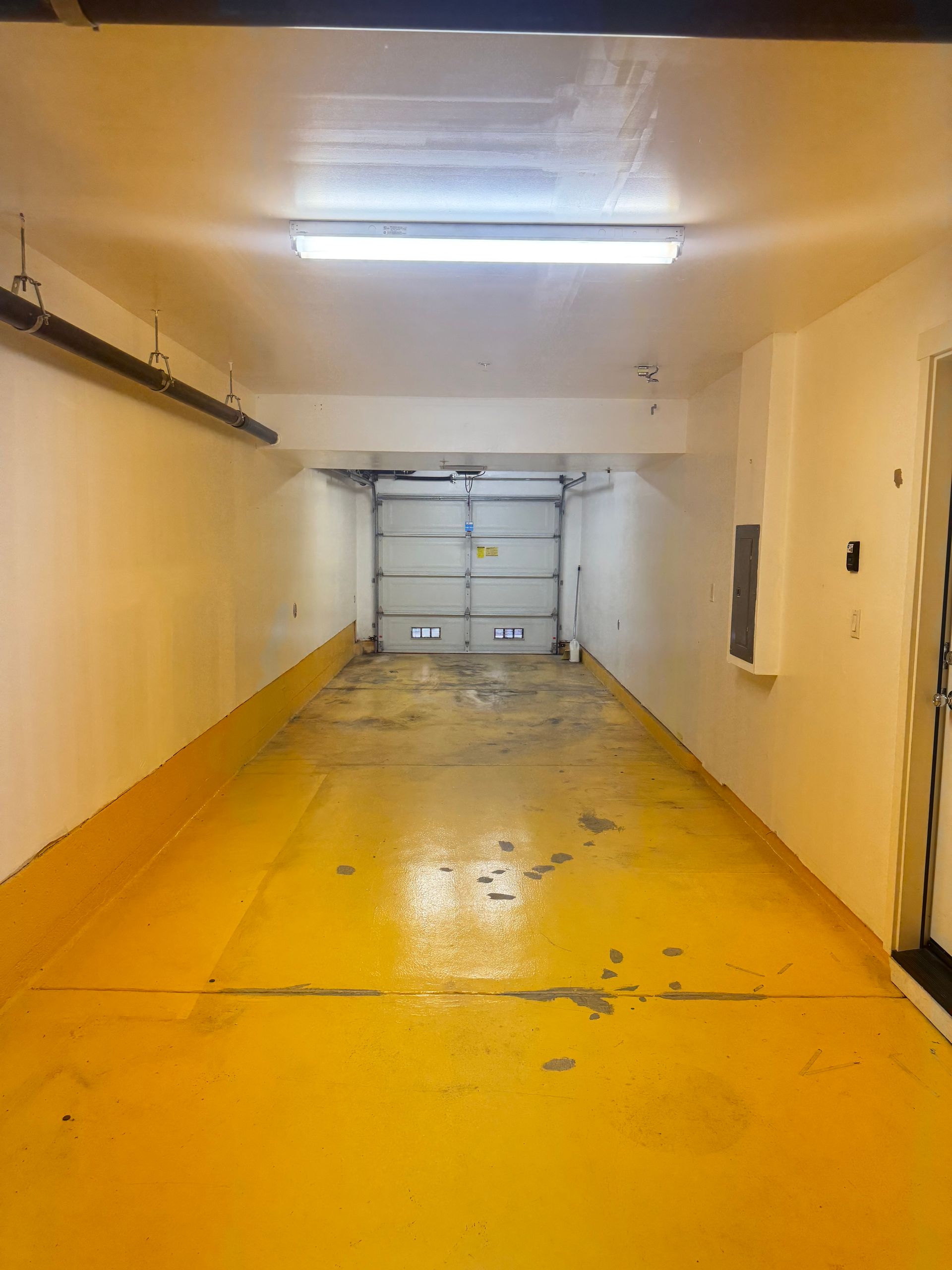 Empty garage with yellow floor, white walls, and a closed garage door.