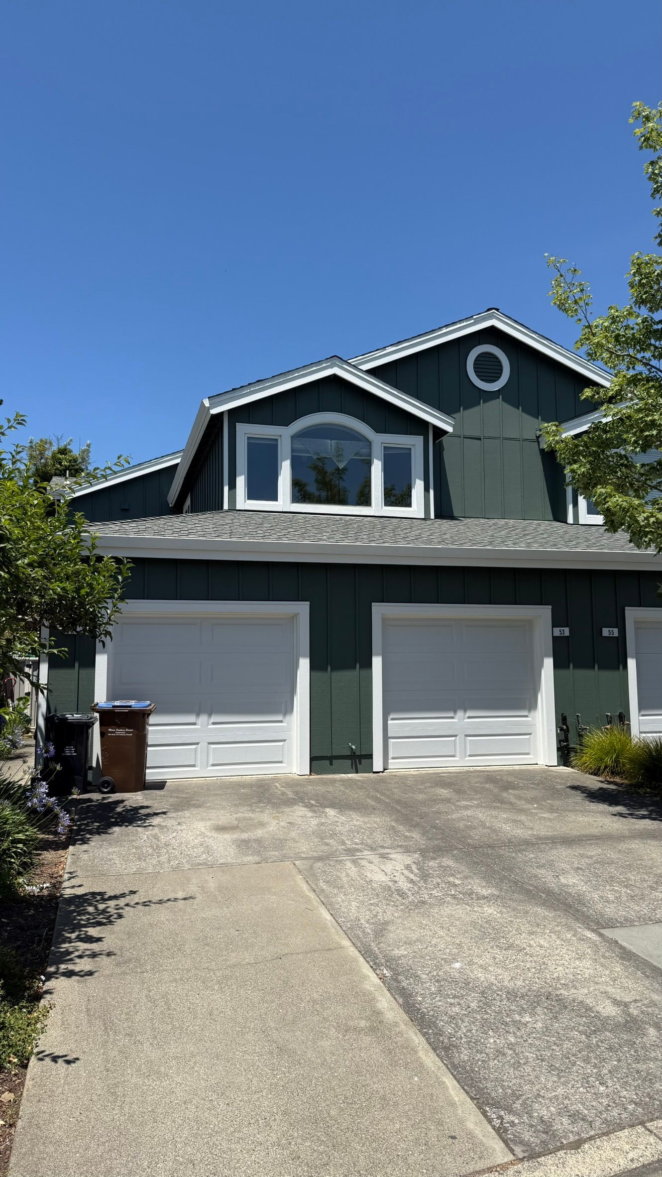 A green house with white garage doors and a blue sky in the background.