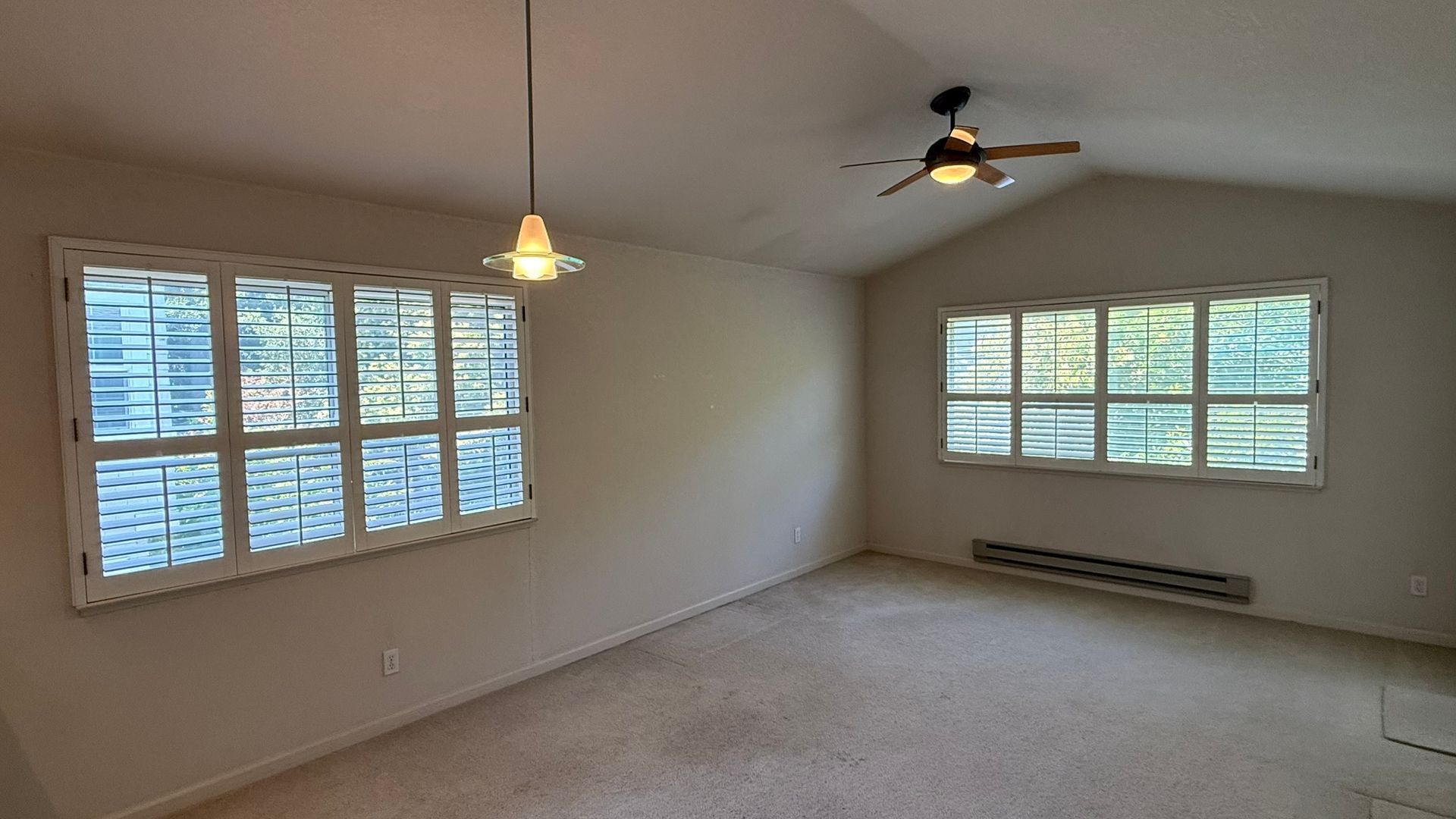 An empty living room with a ceiling fan and lots of windows.