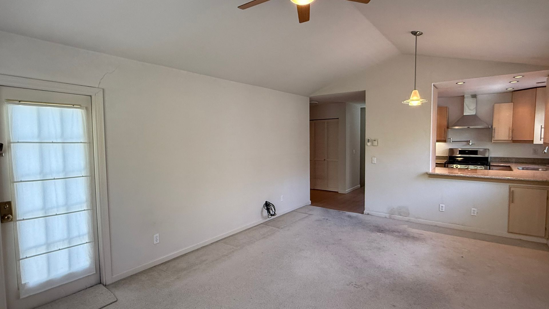 A living room with a ceiling fan and a sliding glass door leading to a kitchen.