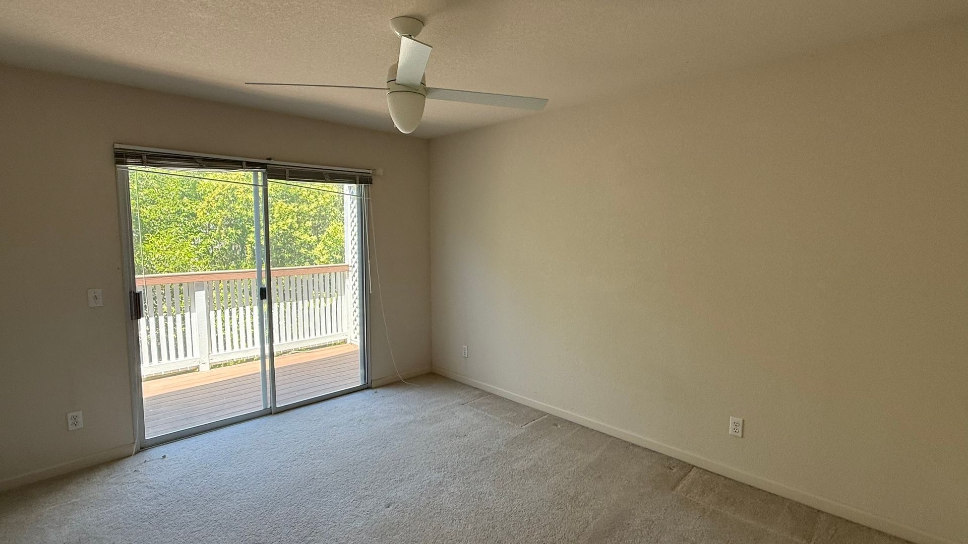 An empty room with a ceiling fan and sliding glass doors leading to a balcony.