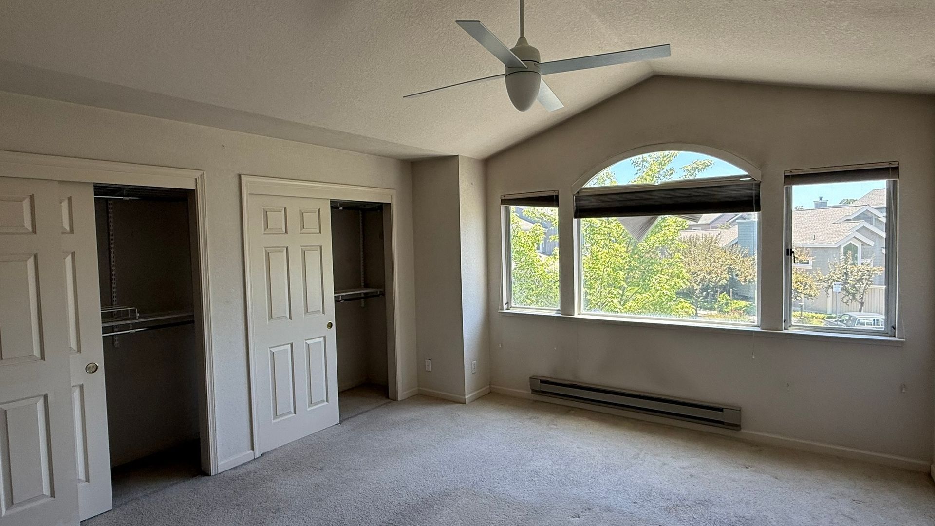 An empty bedroom with a ceiling fan and a large window
