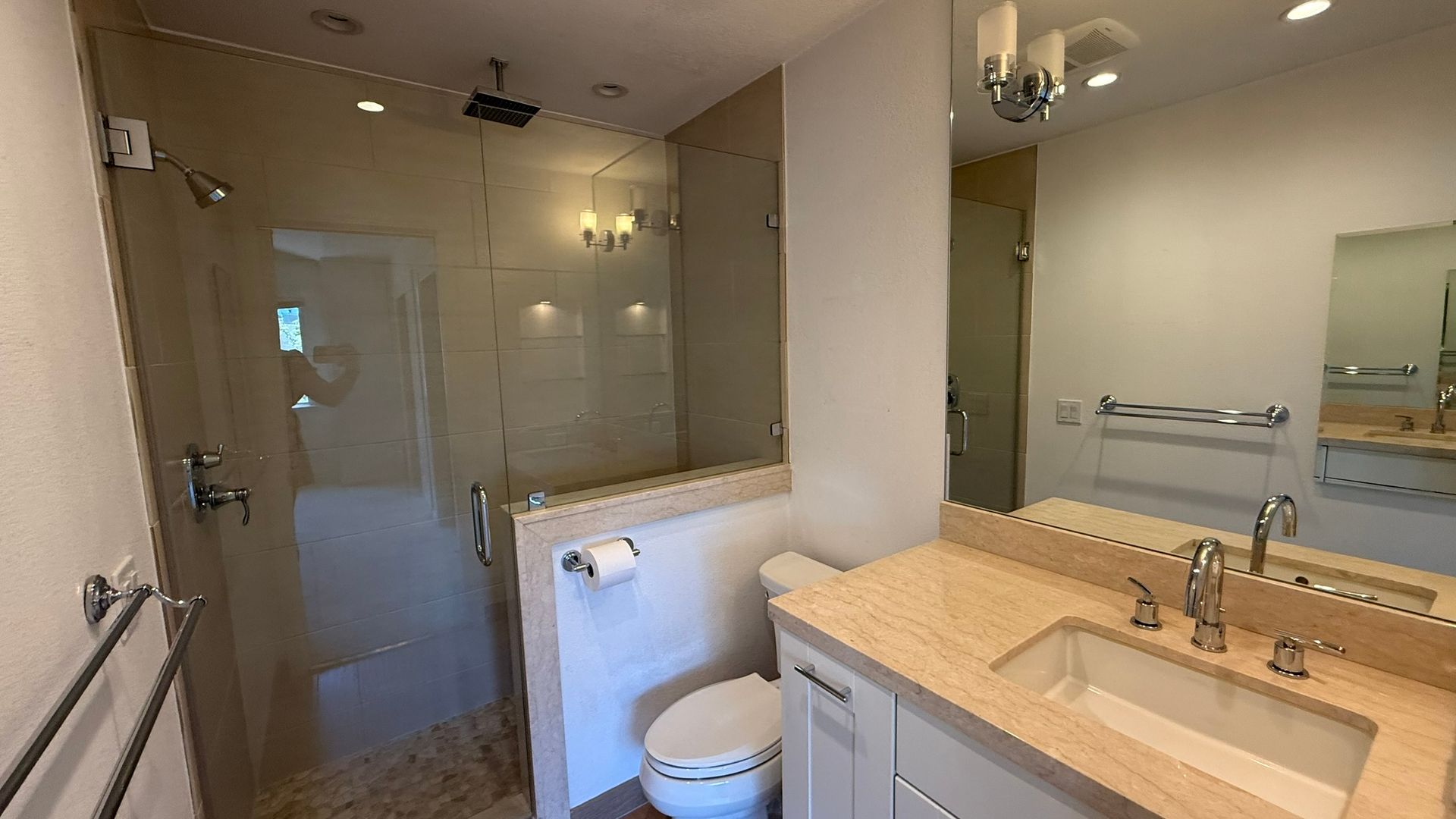 A bathroom with a toilet , sink , shower and mirror.