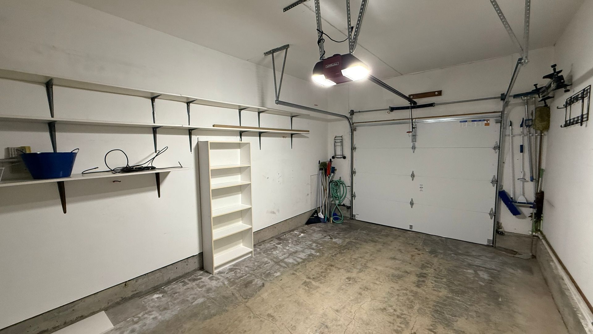An empty garage with a garage door open and shelves.