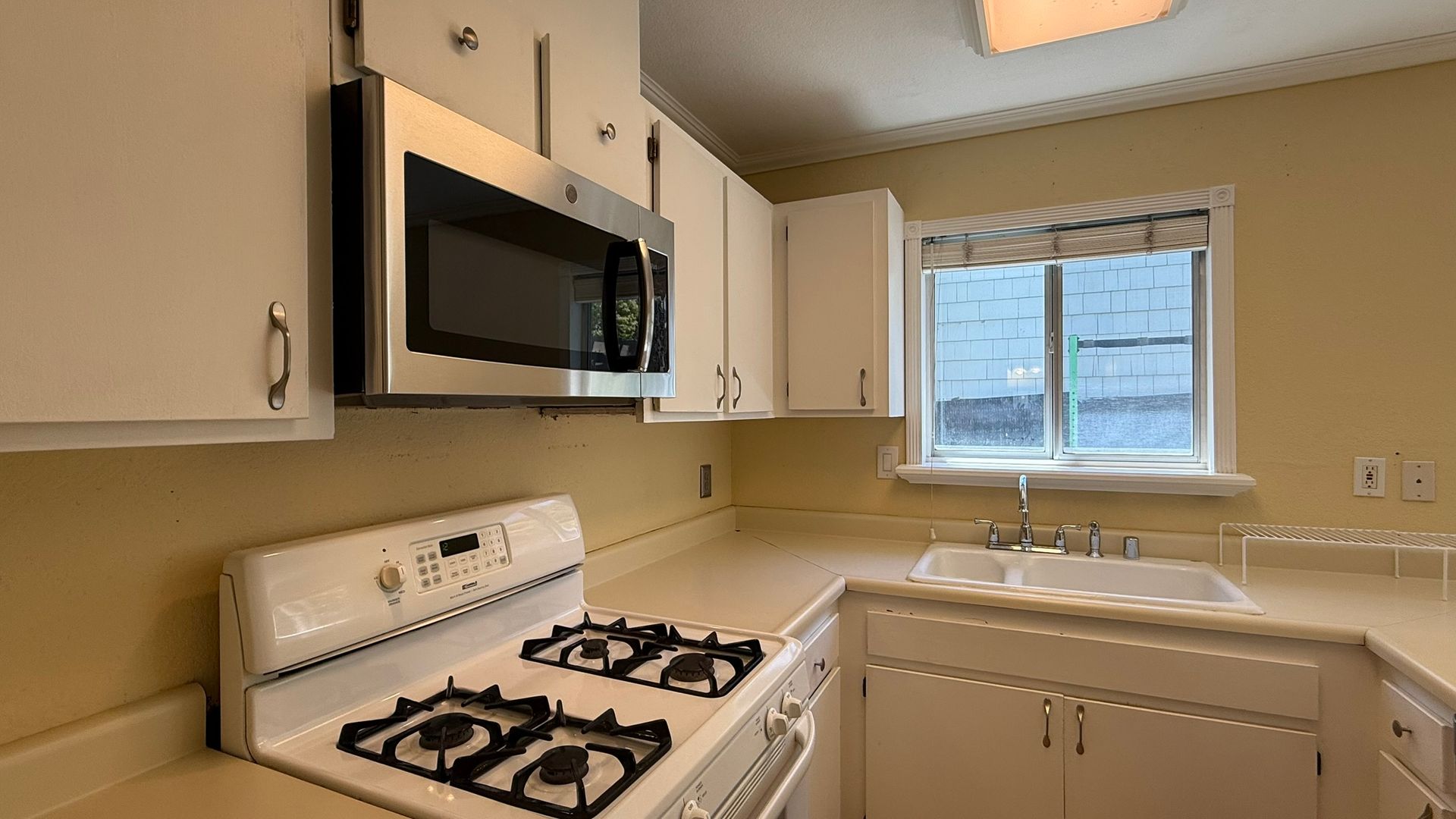 Kitchen with white cabinets, gas stove, microwave, sink, and a window.