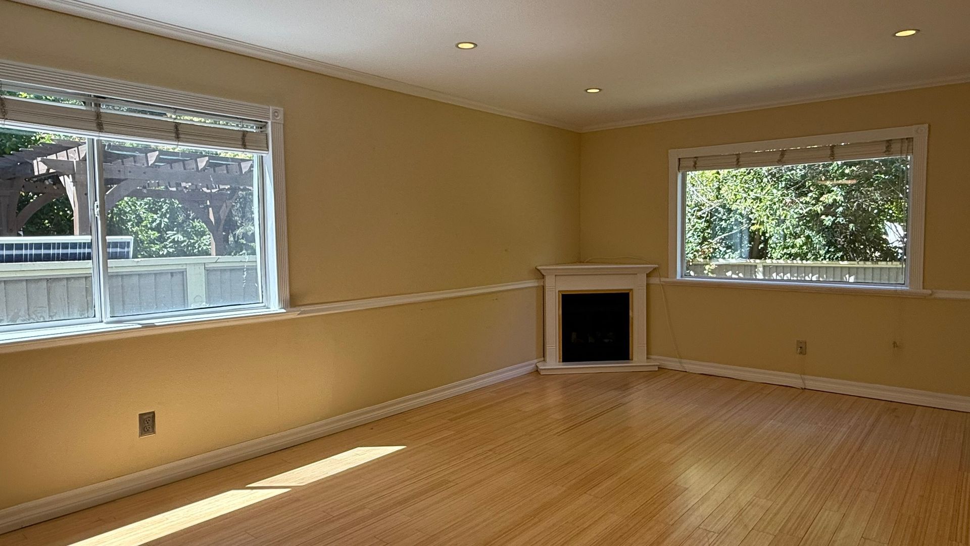 Empty room with wood floors, windows, and a fireplace. Light yellow walls.
