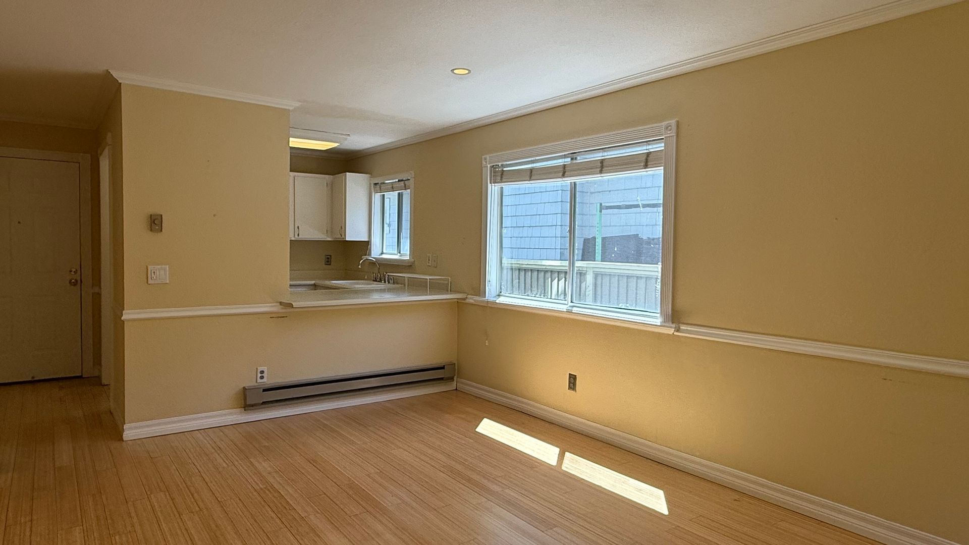 Empty room with light yellow walls, wood floor, and a window overlooking an outdoor area.