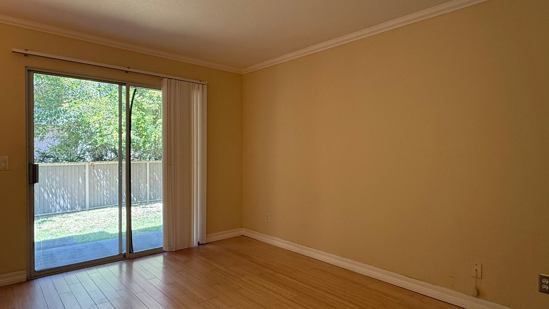 Empty room with a sliding glass door and wooden floors. Beige walls and a glimpse of a backyard.