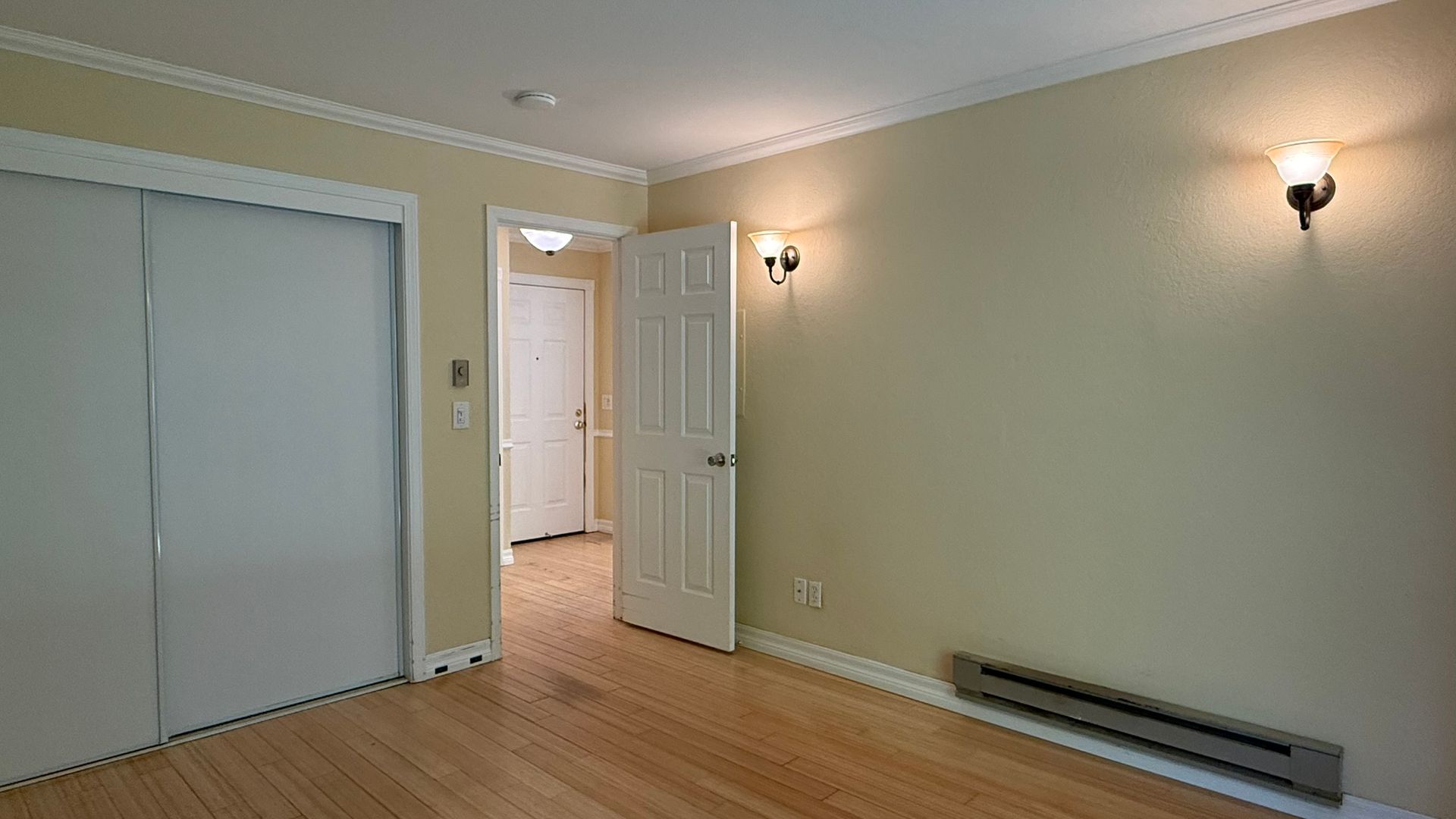 Empty bedroom with closet, door to hallway, sconce lighting, and a baseboard heater.