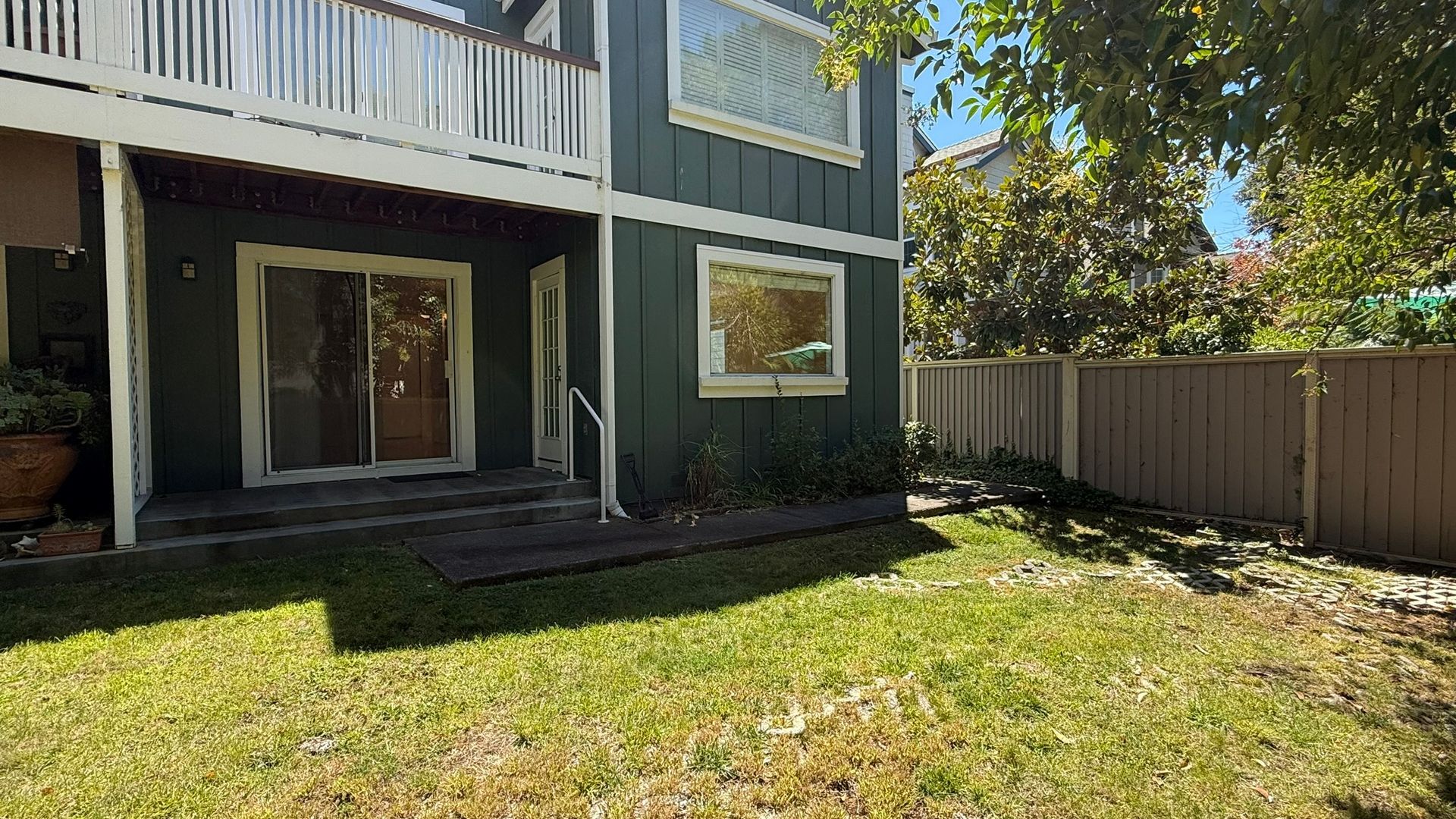 Green house exterior with grass, sliding glass door, and wooden fence.