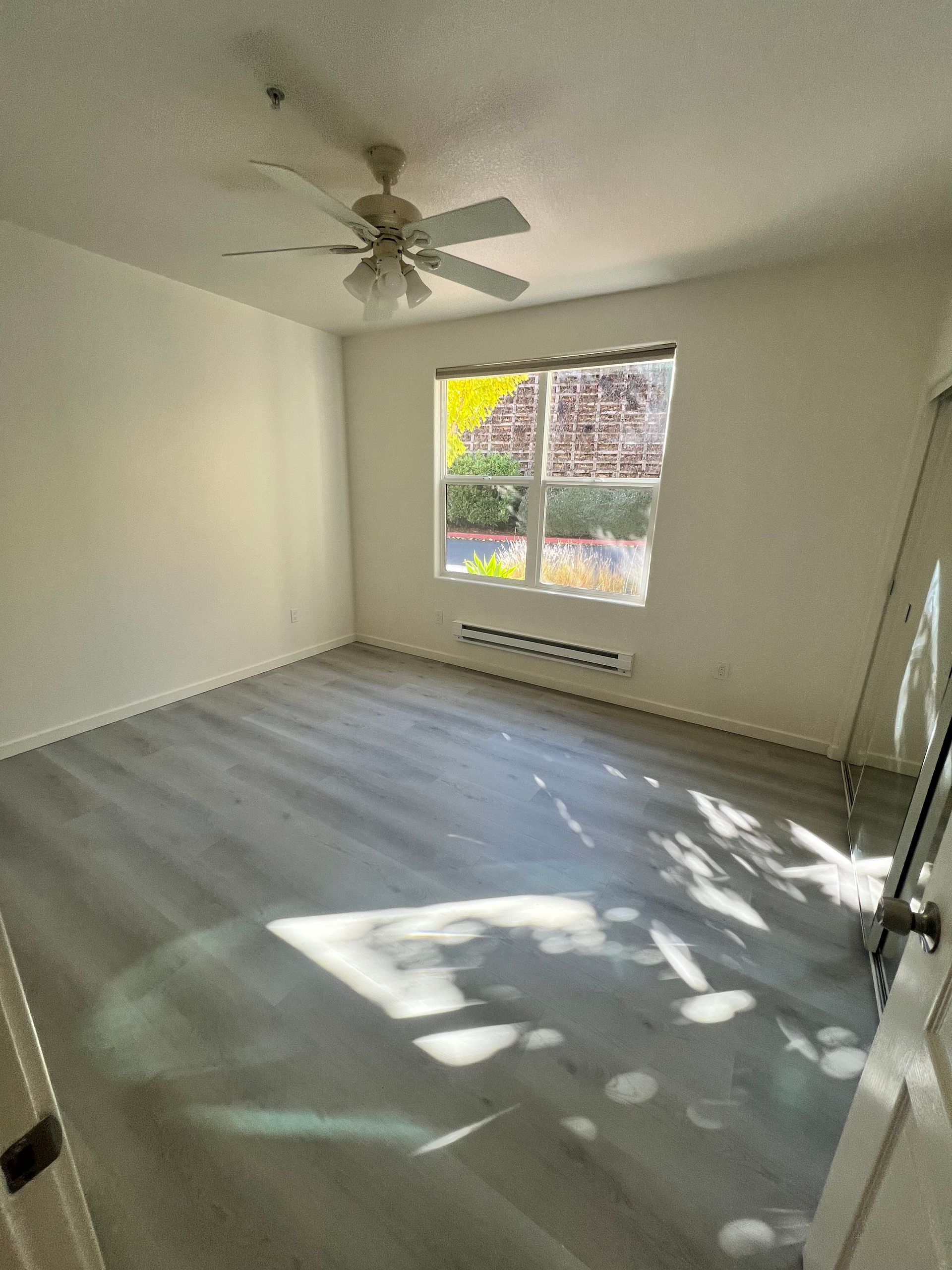 An empty room with a ceiling fan and a window.