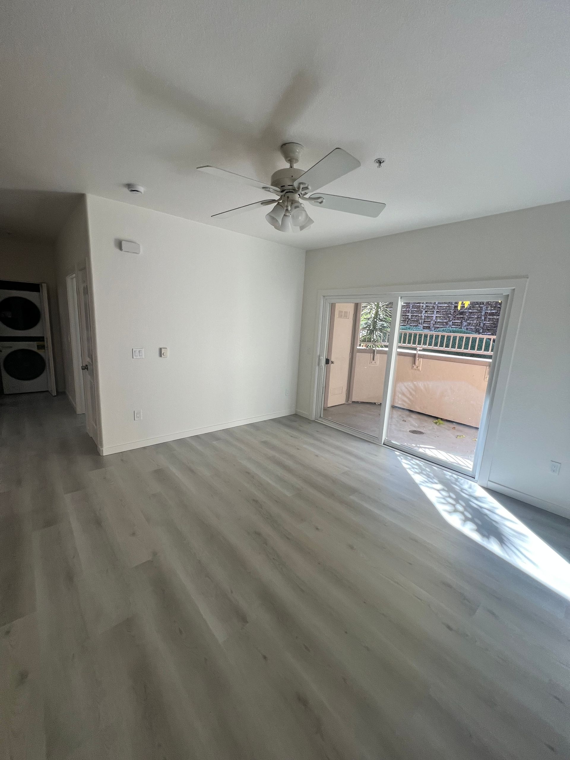 An empty living room with a ceiling fan and sliding glass doors leading to a balcony.