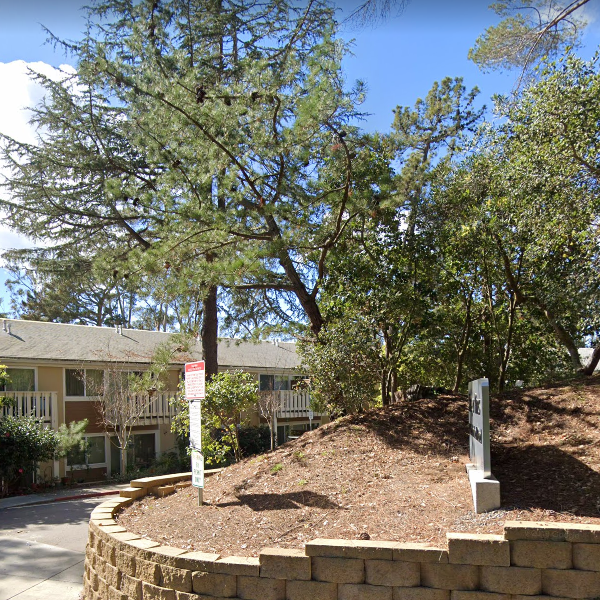 A brick wall is surrounded by trees in front of a building.