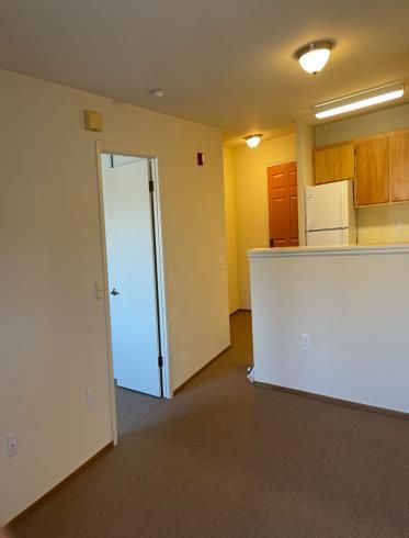 A living room with a refrigerator and a door leading to a kitchen.