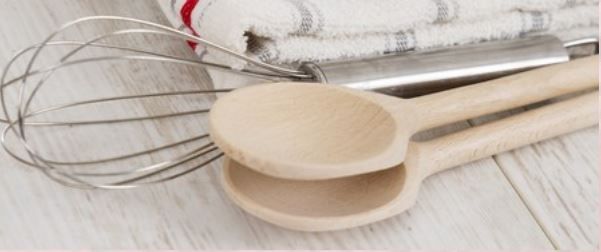 A wooden spoon , measuring cup , and whisk on a wooden table.