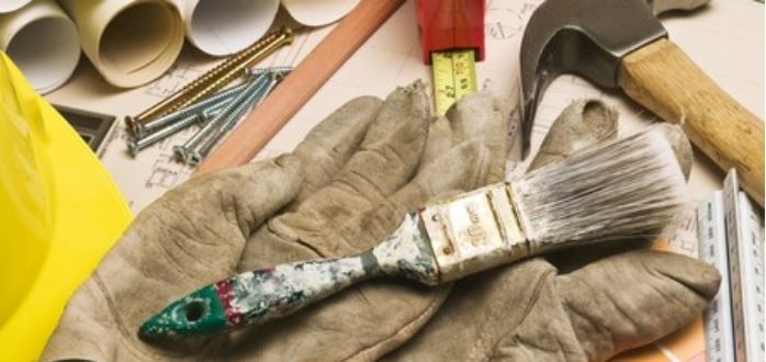 A pair of gloves holding a paint brush on a table with tools.