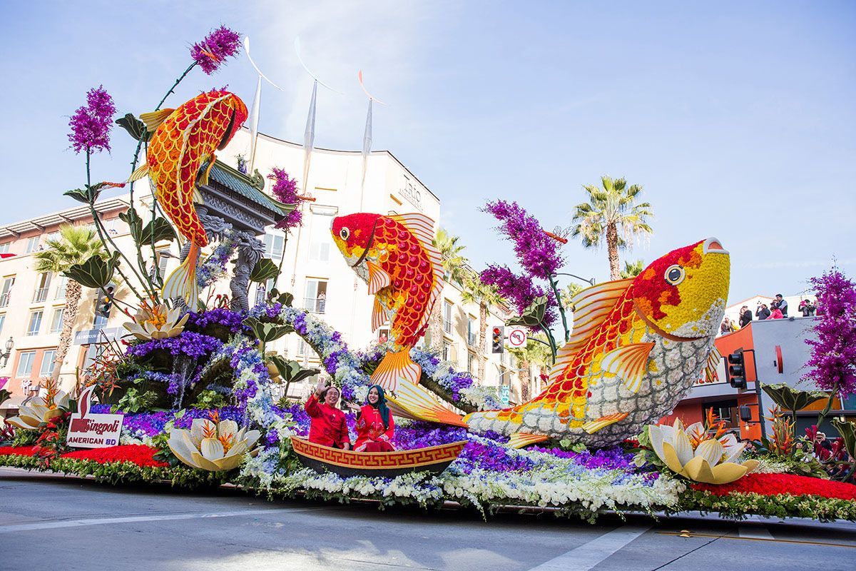 Rose parade float with large koi fish made of flowers; city backdrop.
