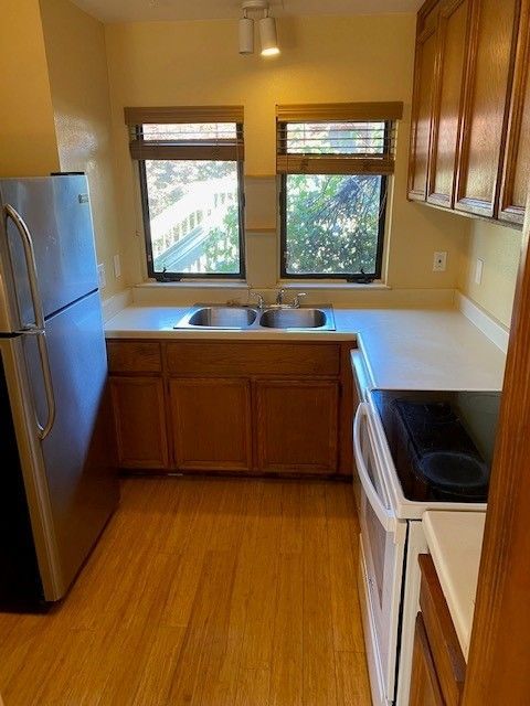 A kitchen with a refrigerator , stove , sink and two windows.