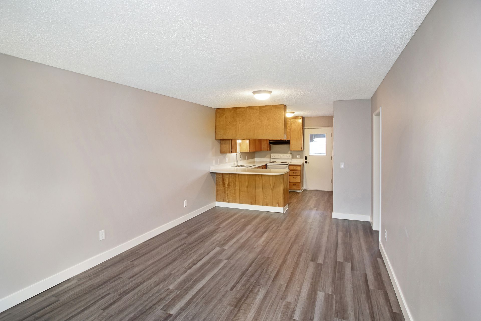 A living room with hardwood floors and a kitchen in the background.