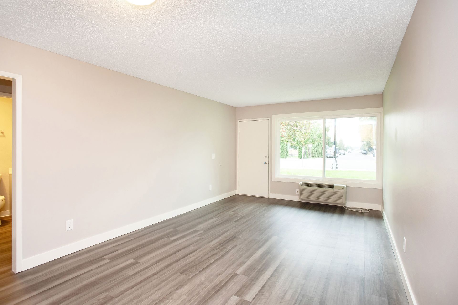 An empty living room with hardwood floors and a large window.