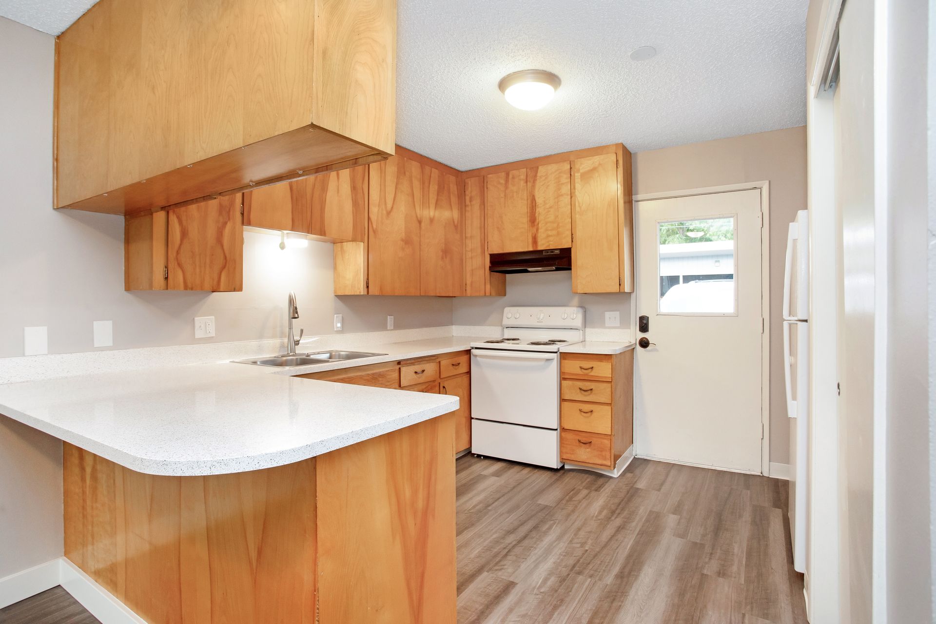A kitchen with wooden cabinets , a white stove , a sink , and a refrigerator.
