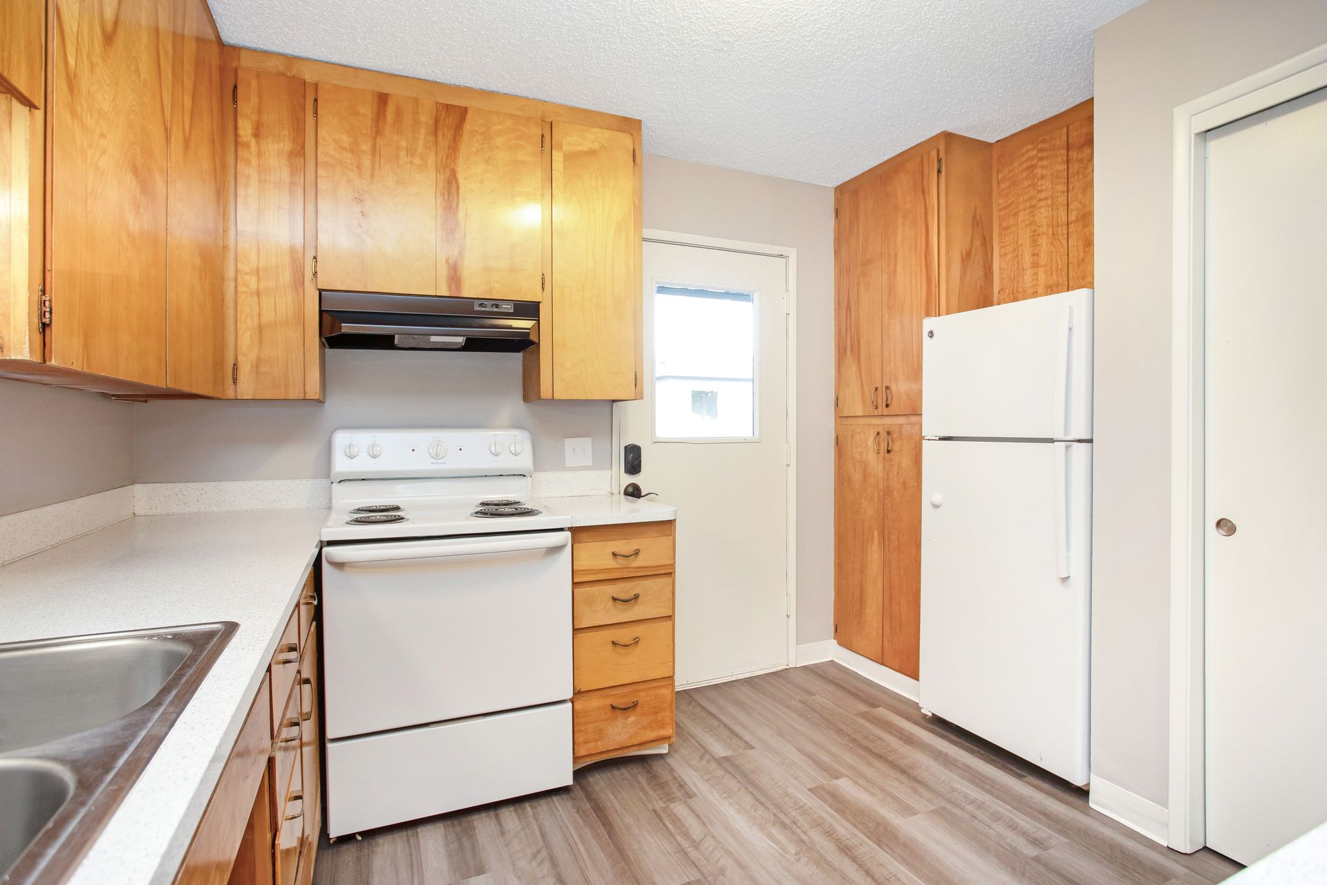 A kitchen with a stove , refrigerator , sink and wooden cabinets.