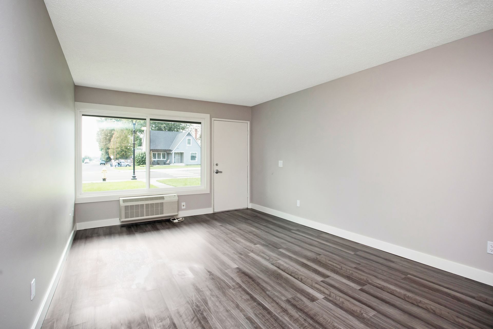 An empty living room with hardwood floors and a large window.