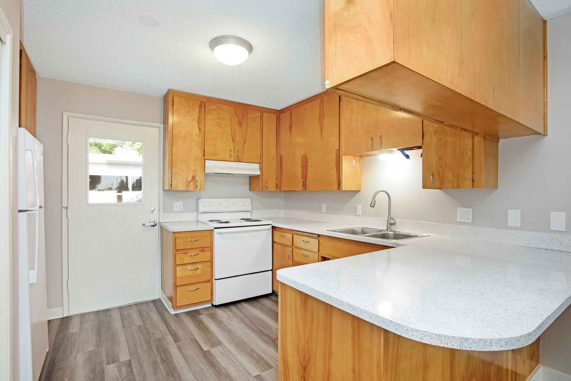 A kitchen with wooden cabinets , a white stove , a sink , and a refrigerator.