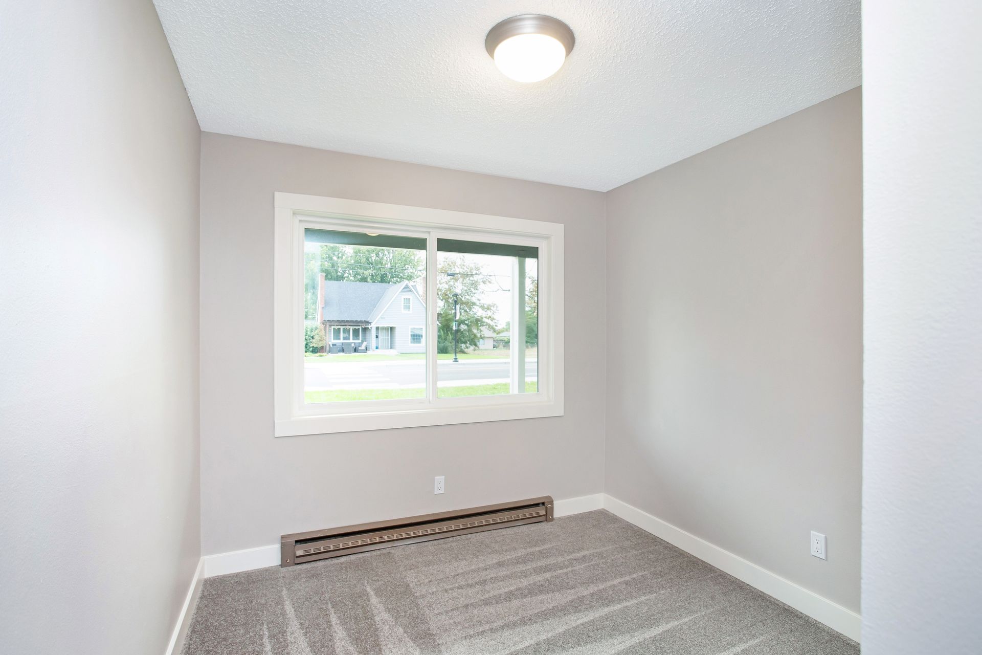 An empty bedroom with a large window and a rug.
