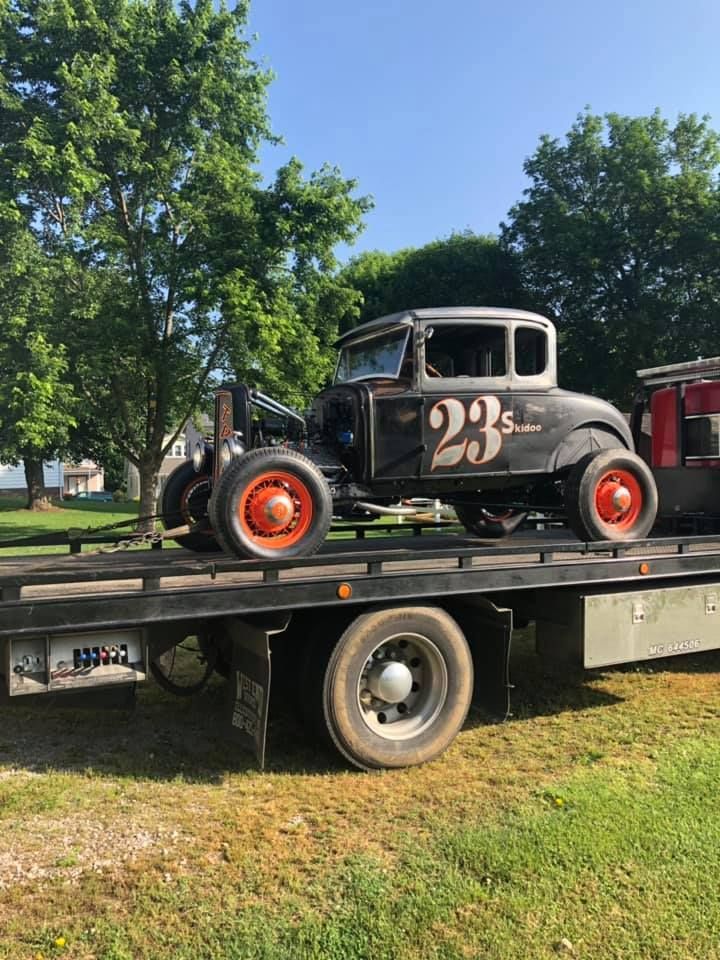 A white truck is towing a red tractor on a trailer.