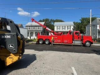 A man in a blue jumpsuit is walking towards a broken down car.