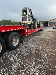 A semi truck is carrying a green tractor down a highway.