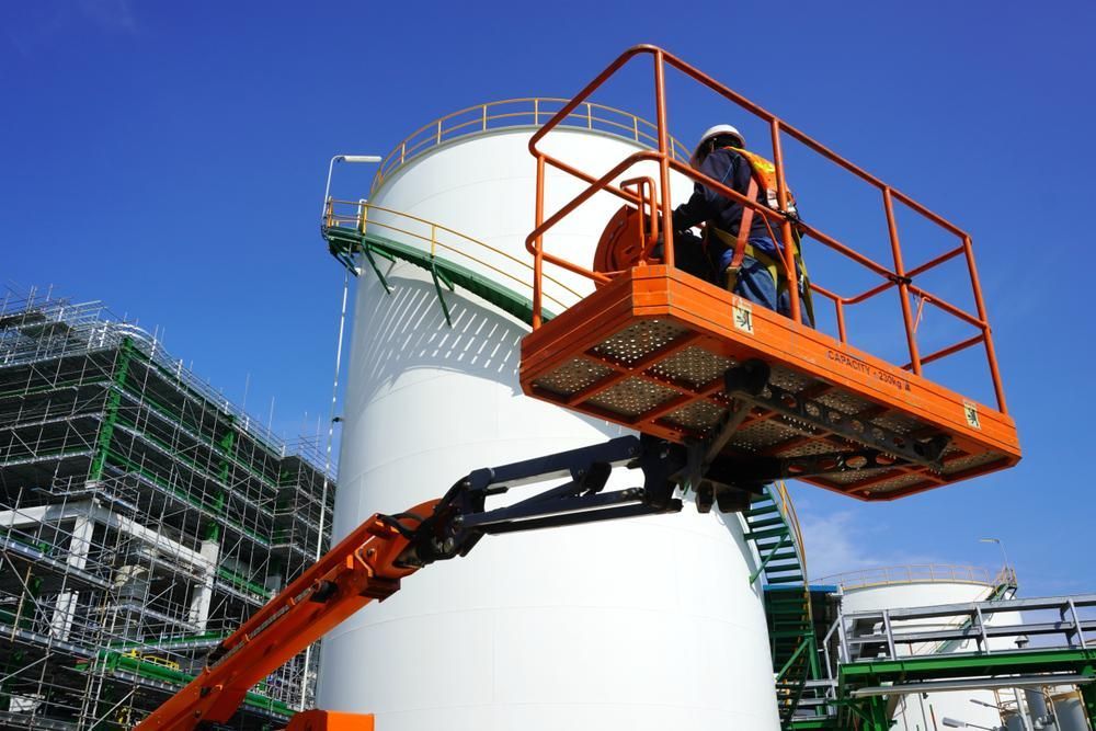 A Man Is Standing on A Lift in Front of A Large White Tank — AMAC Cranes in Coolum Beach, QLD