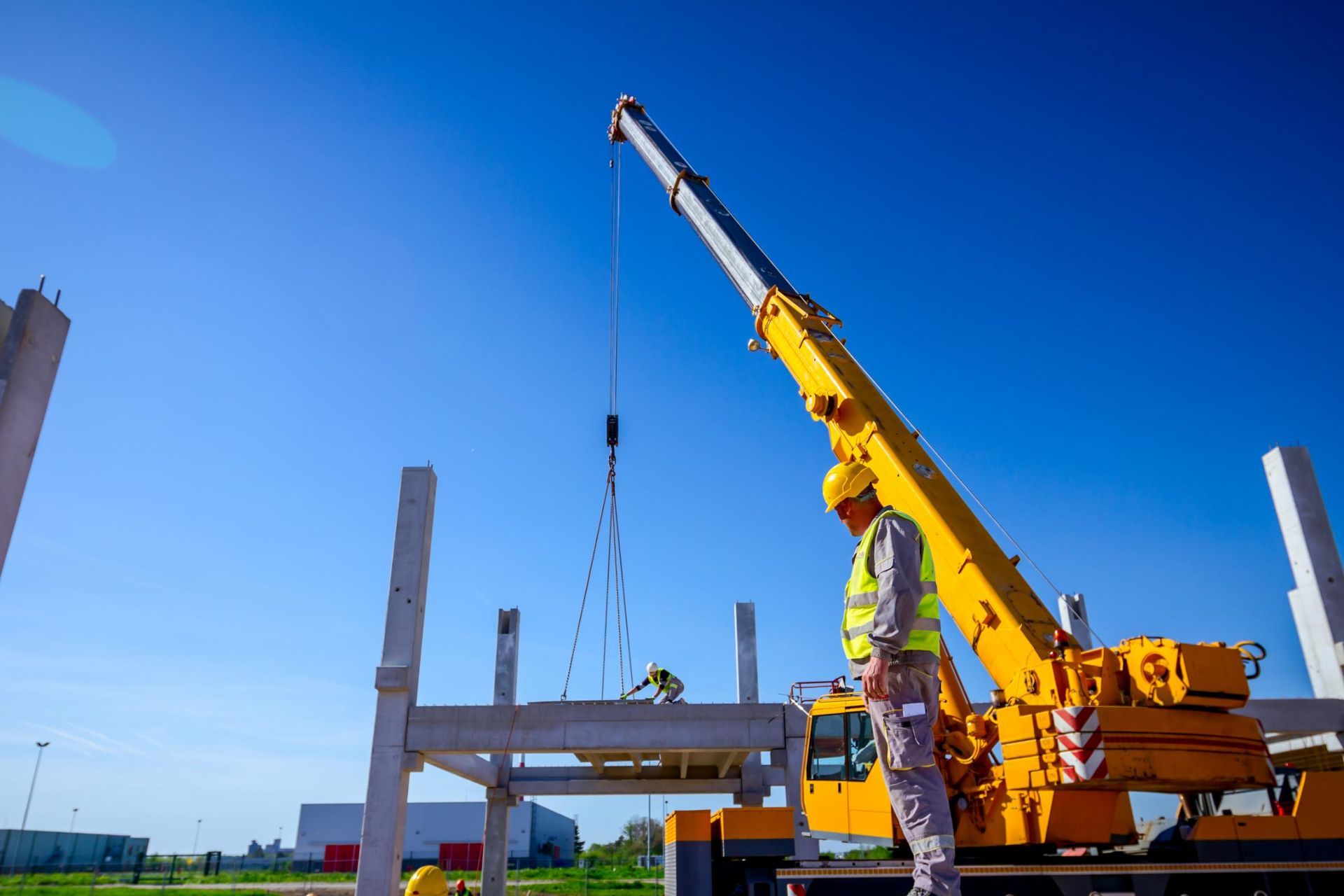 A Construction Worker Is Standing Next to A Yellow Crane at A Construction Site — AMAC Cranes in Coolum Beach, QLD