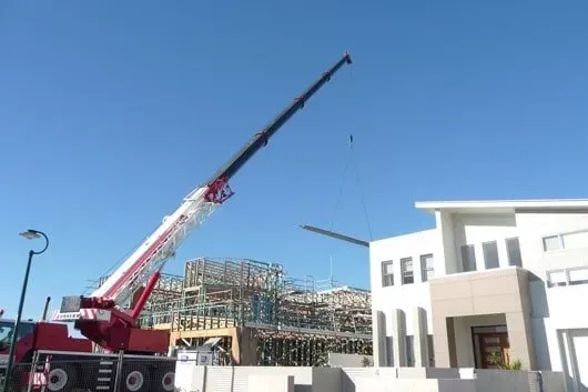 A Red and White Crane Is Sitting in Front of A Building Under Construction — AMAC Cranes in Coolum Beach, QLD