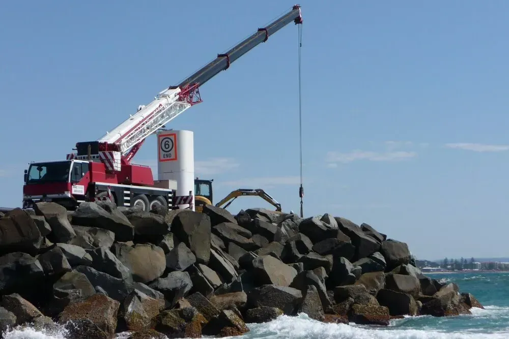 A Large Crane Is Sitting on Top of A Pile of Rocks Near the Ocean — AMAC Cranes in Coolum Beach, QLD