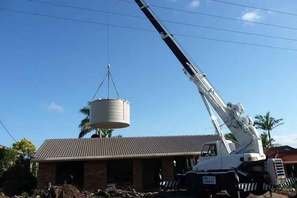 A Large White Crane Is Lifting a Circular Object Over a House — AMAC Cranes in Coolum Beach, QLD