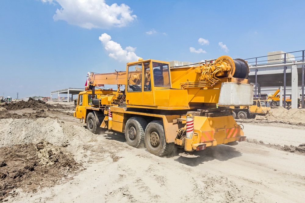 A Yellow Crane Is Driving Down a Dirt Road at A Construction Site — AMAC Cranes in Coolum Beach, QLD